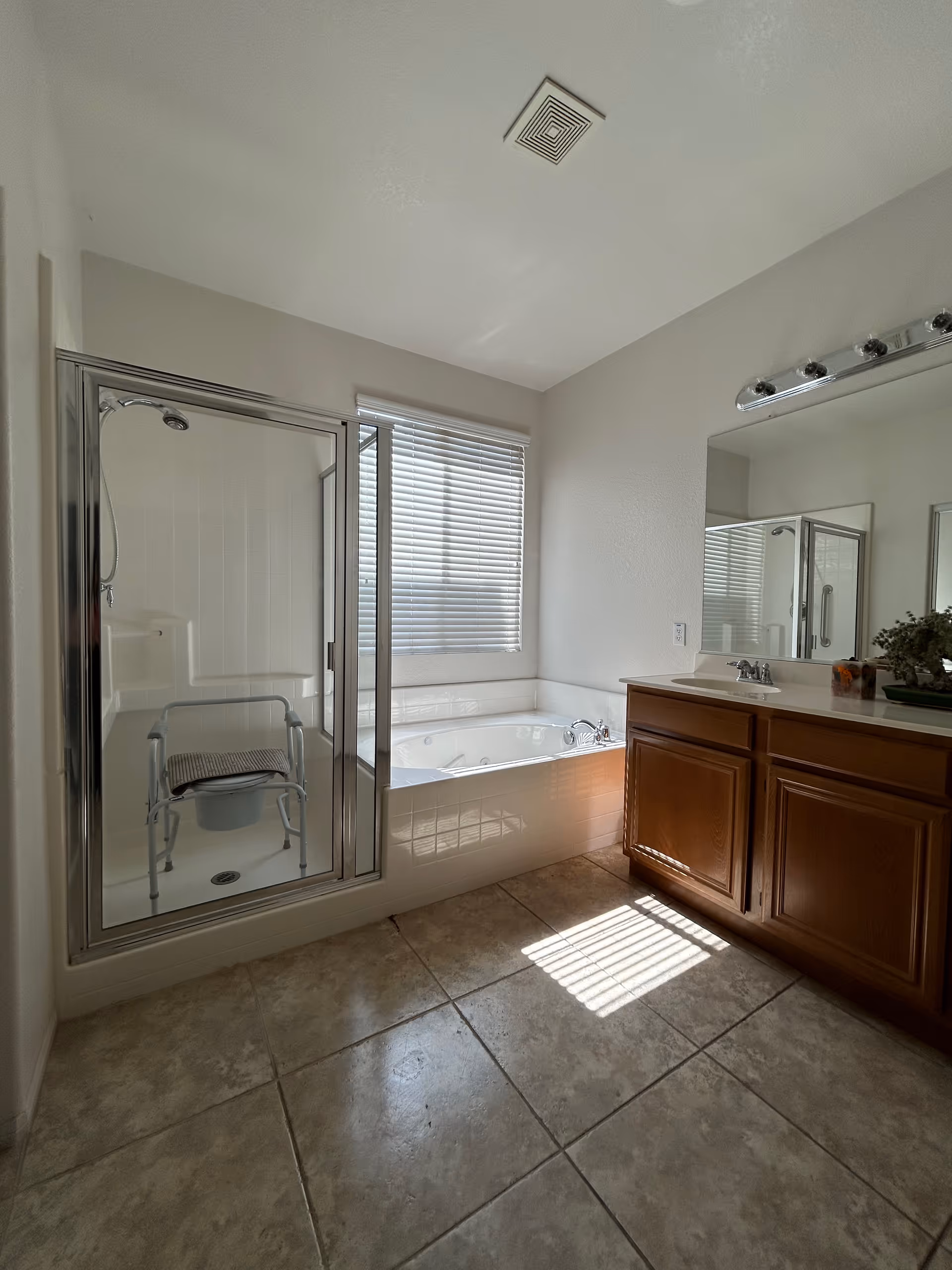 A bathroom with a glass shower, bathtub, tile floor, and wooden vanity.