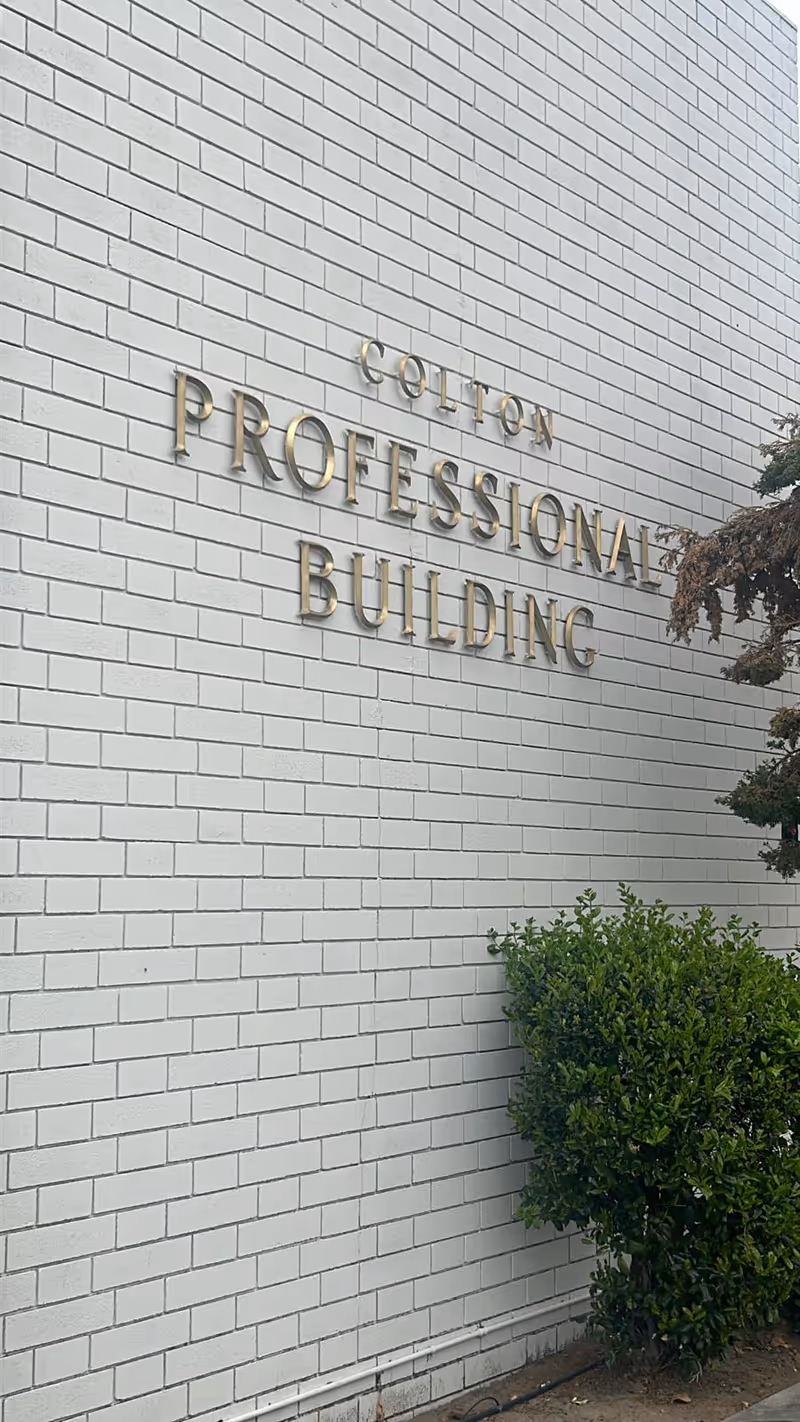 Exterior white brick wall with gold signage reading Professional Building and greenery.