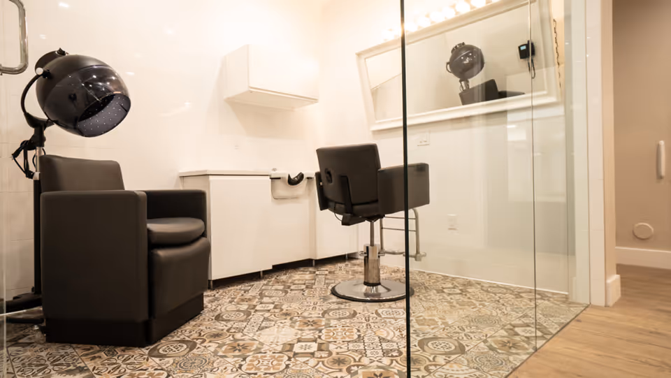 Modern hair salon inside facility with a hooded dryer chair, mirror, glass partition, patterned floor