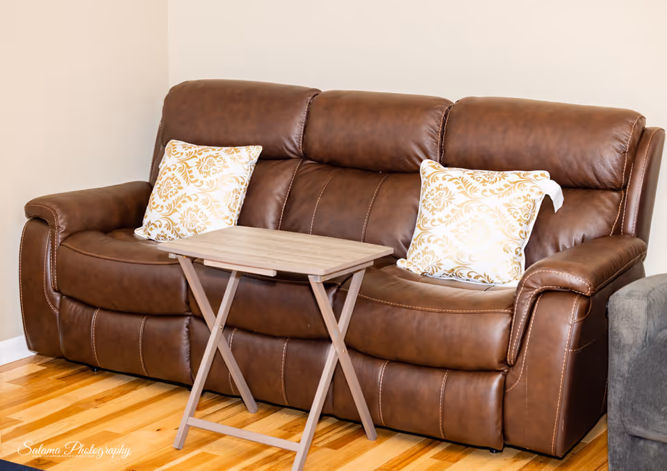 Brown leather sofa with patterned cushions and a small wooden folding table in a living room.