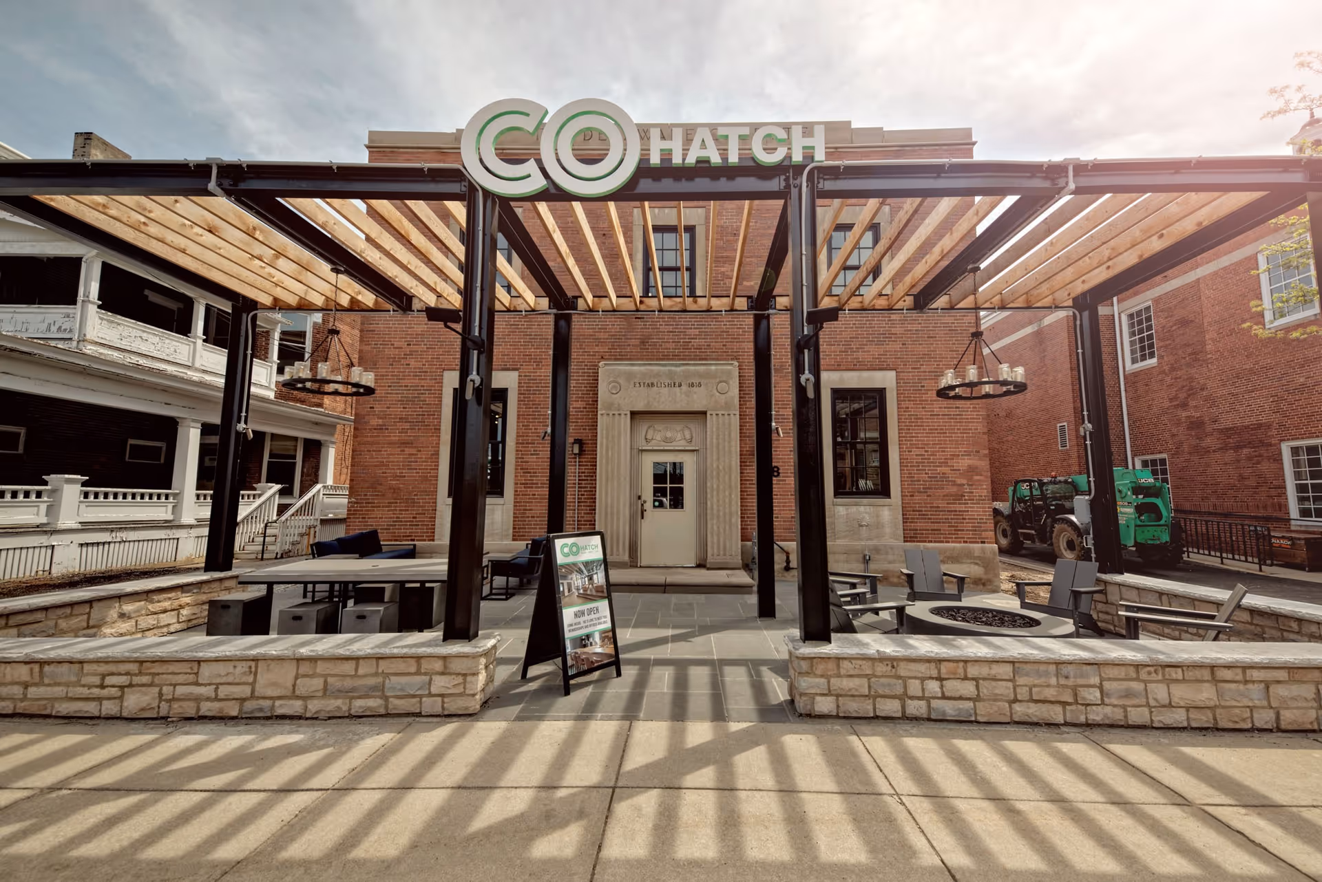 Brick building entrance with pergola-covered outdoor seating and a CoHatch sign.