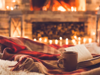 Cozy living room with a lit fireplace, blanket, mug, and a book.