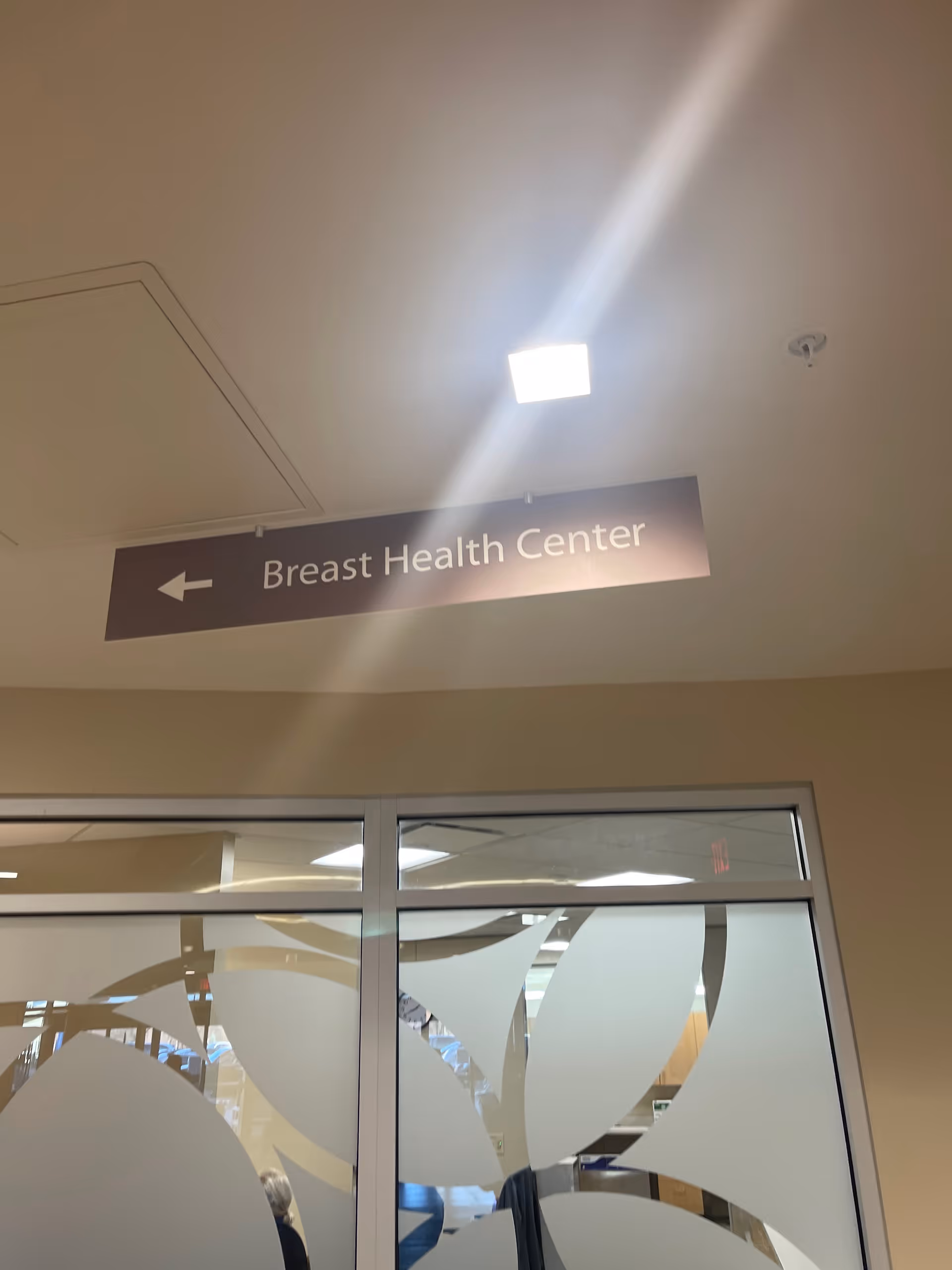 Interior hospital corridor with a sign reading Breast Health Center and frosted glass doors.