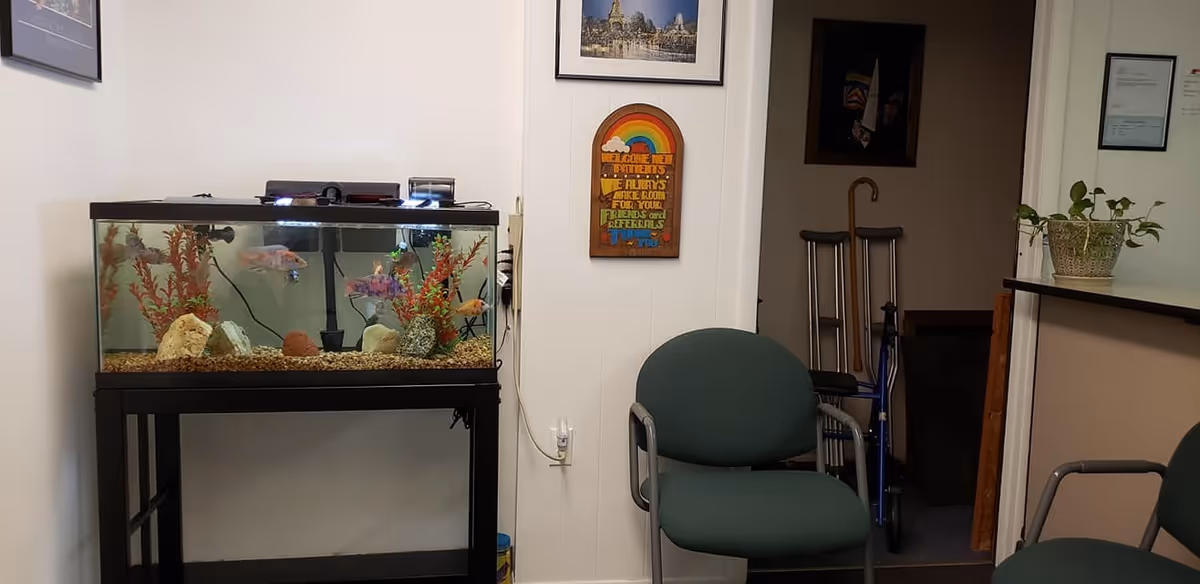 Indoor lounge area featuring an aquarium, green chairs, and a hallway with crutches in the background.
