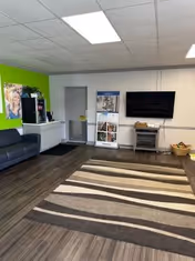 Indoor waiting area with green accent wall, couch, brochure stand, TV, and striped rug.