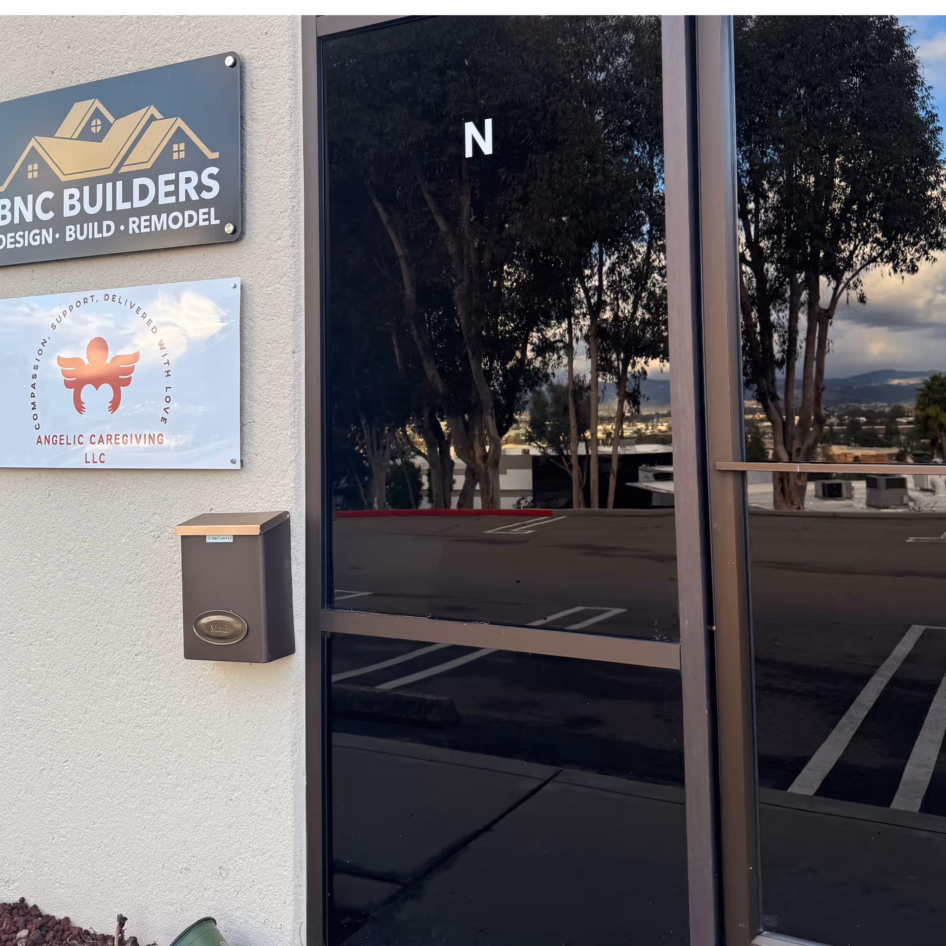 Exterior of building entrance with Angelic Caregiving LLC sign and glass doors reflecting trees.