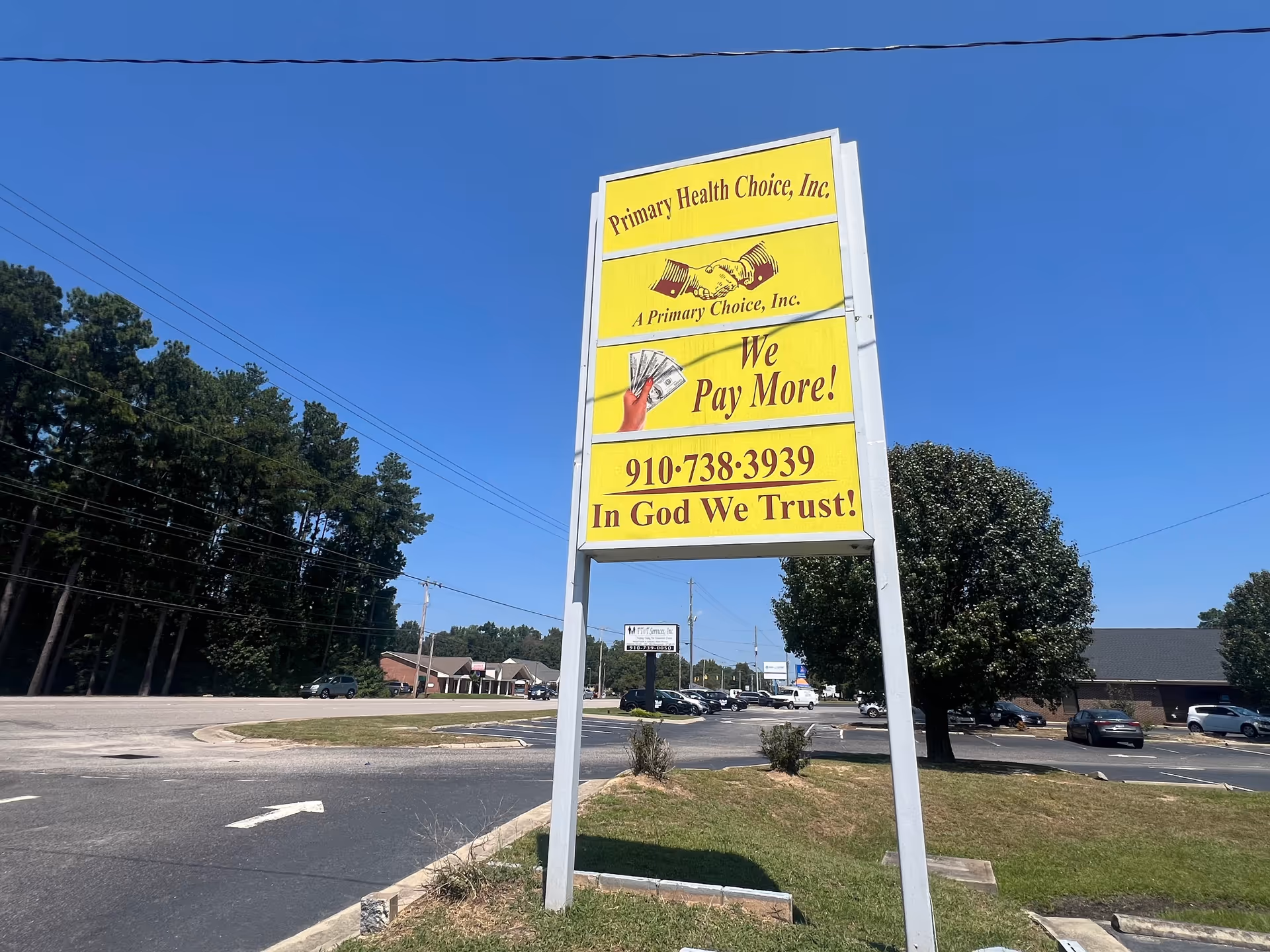 Tall yellow Primary Health Choice sign in a parking lot with trees.