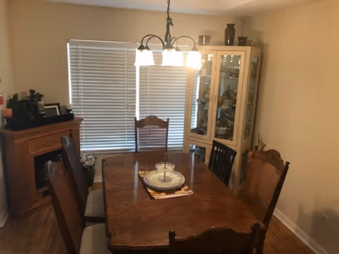 Wood dining table and chairs in a dining room with a glass cabinet and chandelier.