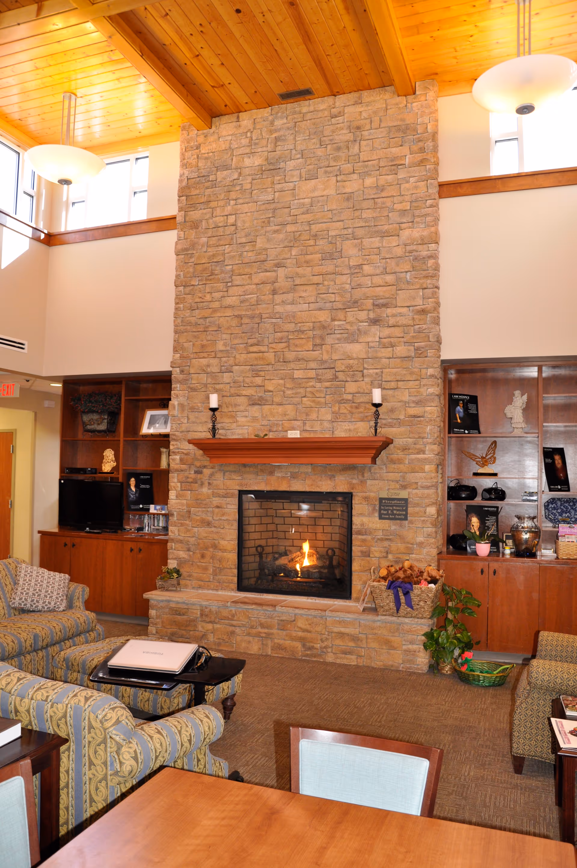 Stone fireplace dominates a cozy living room with couches, shelves, and warm lighting.