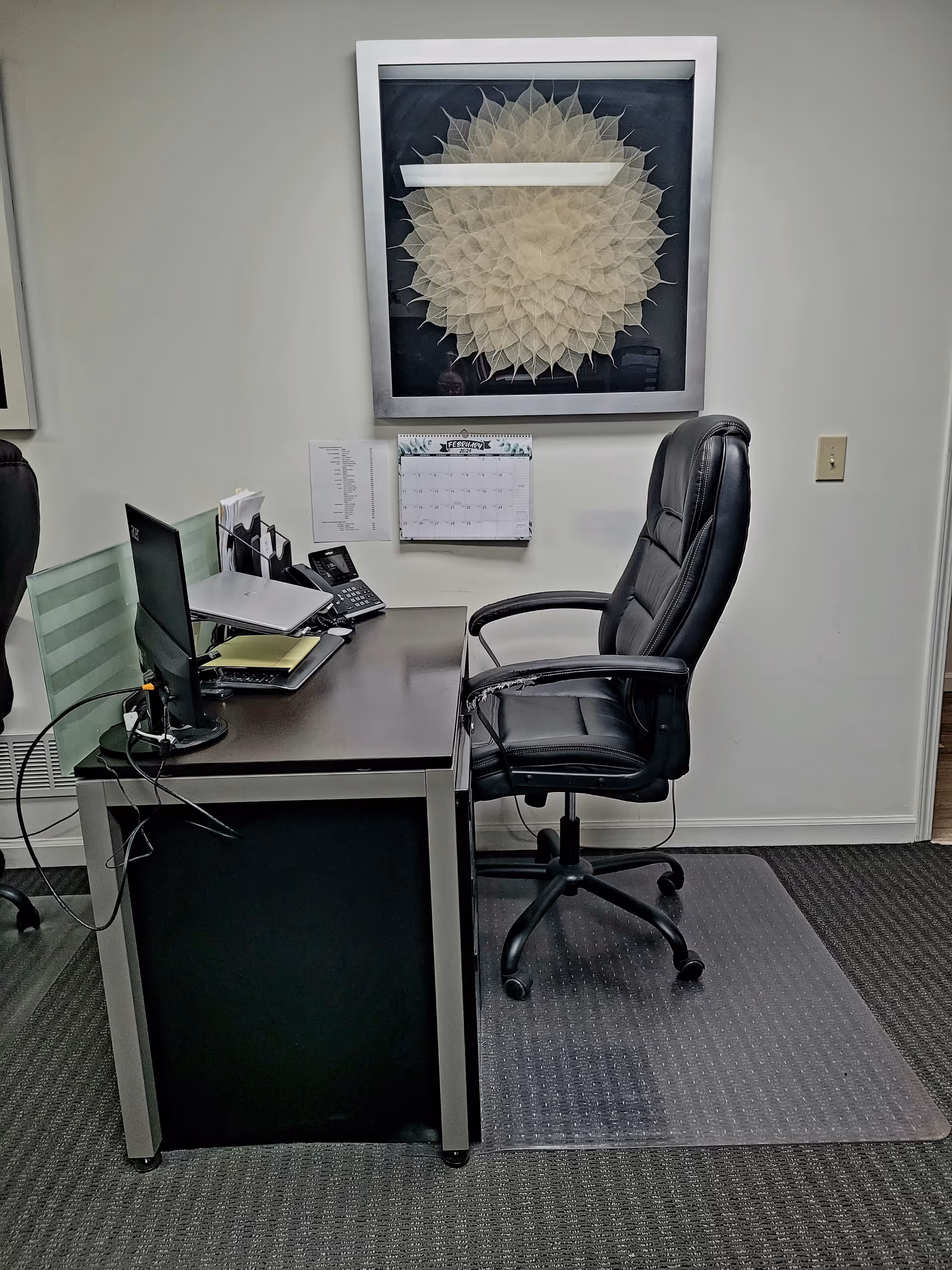 An office desk with computer, phone, and calendar in a furnished senior facility workspace.