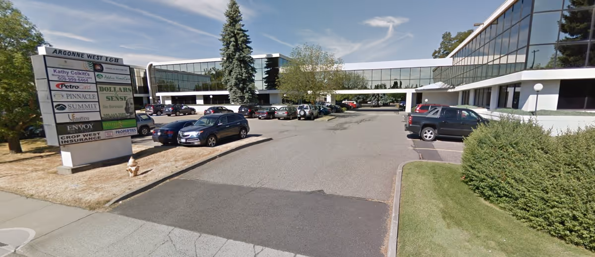 Exterior view of a modern glass-fronted building with a parking lot and landscaping.