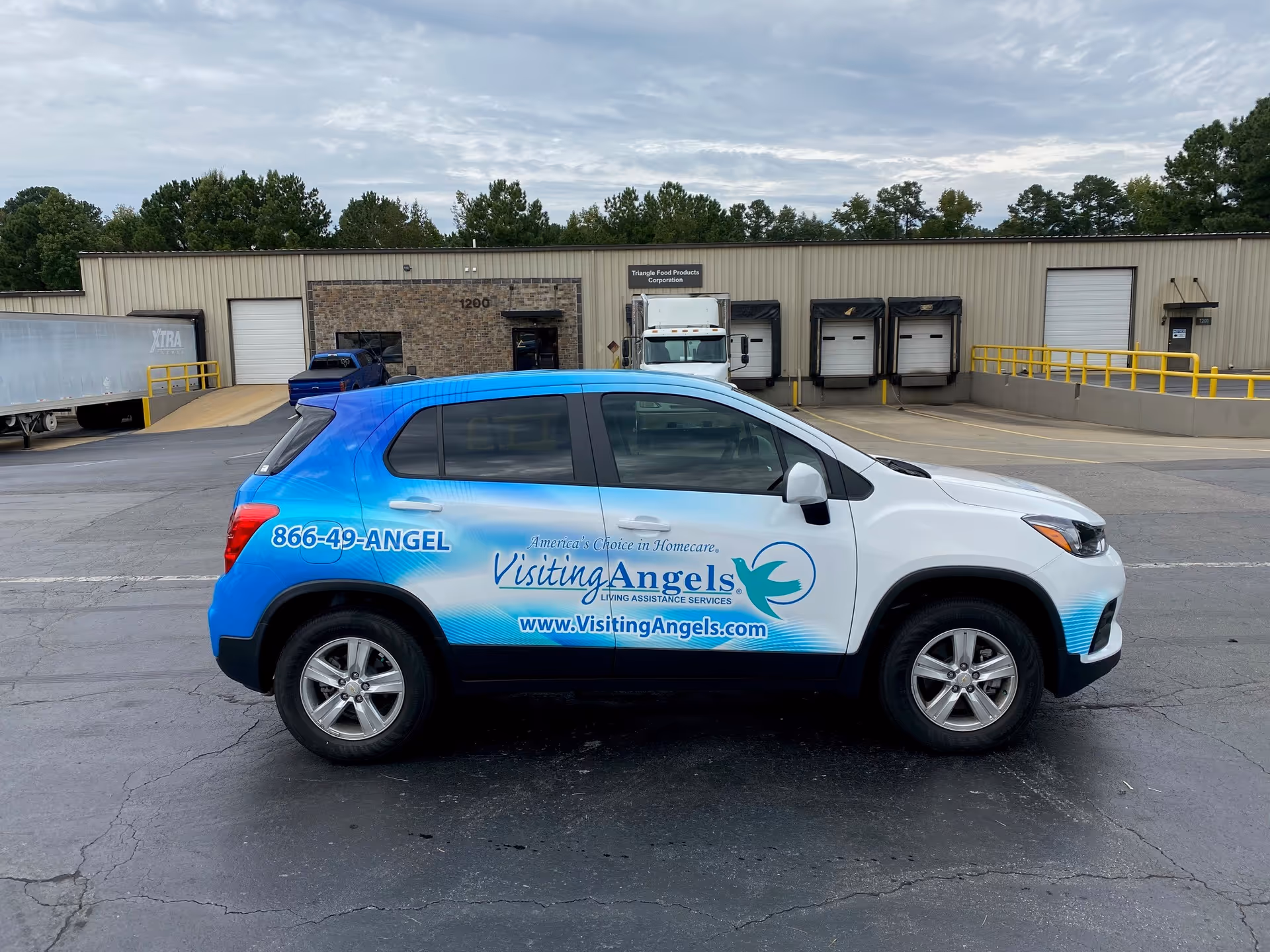 Blue and white Visiting Angels care van parked outside a loading dock facility.