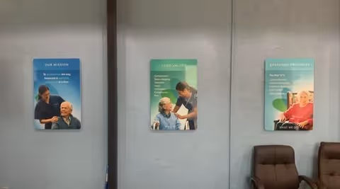 Gray wall with three informational posters and two brown chairs in a waiting area.