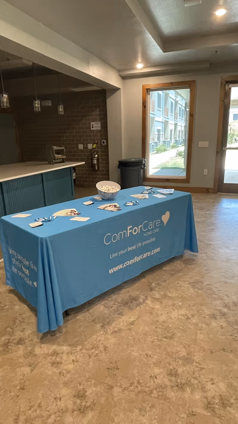 Blue ComForCare promotional table indoors in a lobby area with doorway and logo