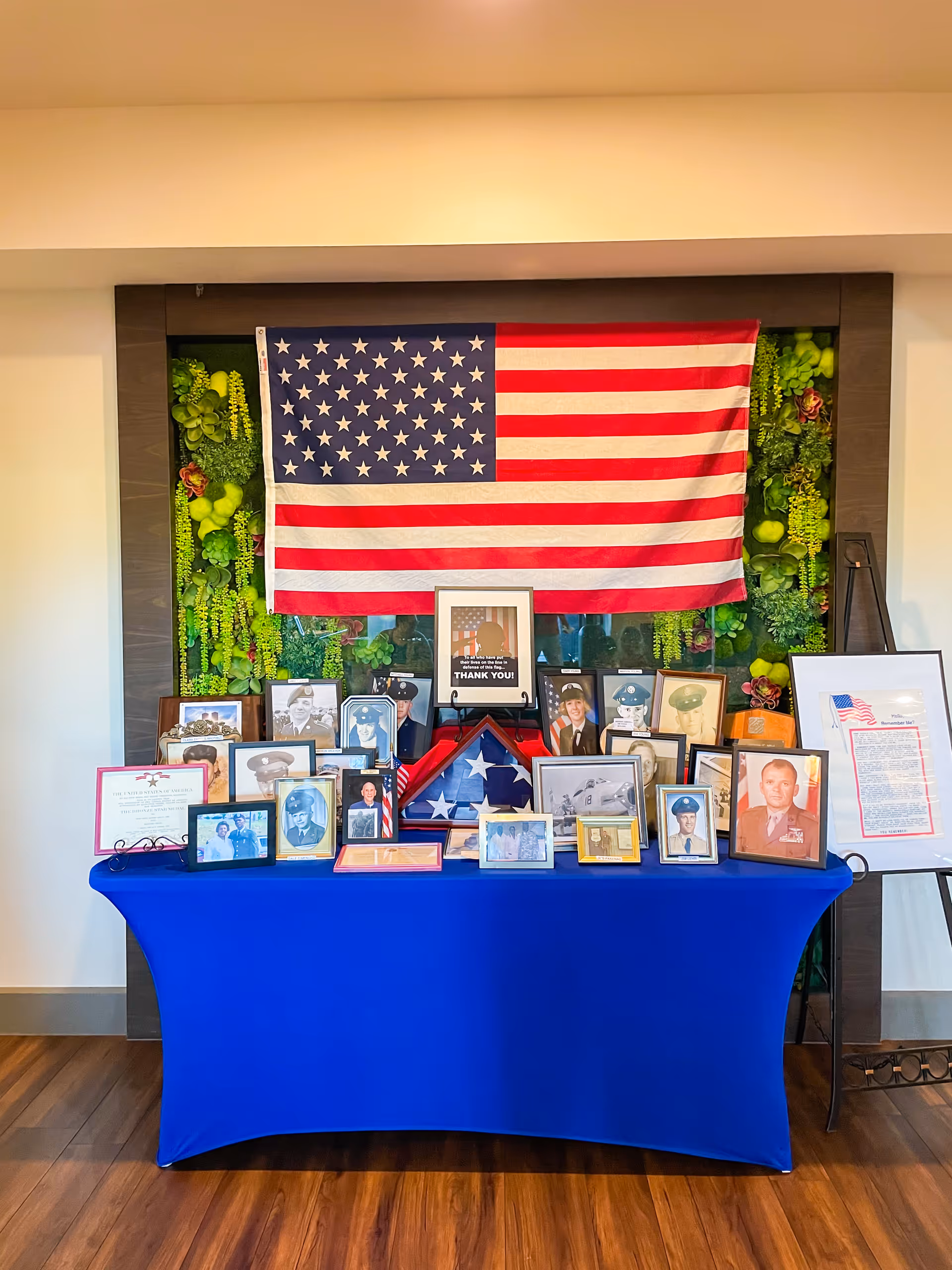 American flag displayed above a table of framed veterans' photos in a Senior Helpers lobby.