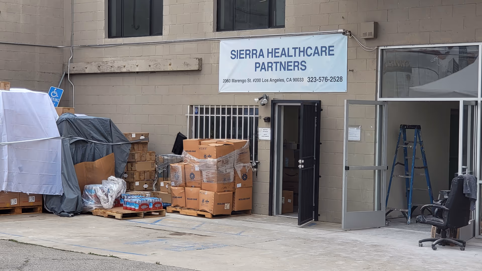 Exterior view of Sierra Healthcare Partners facility with loading docks, stacked boxes, and a banner.