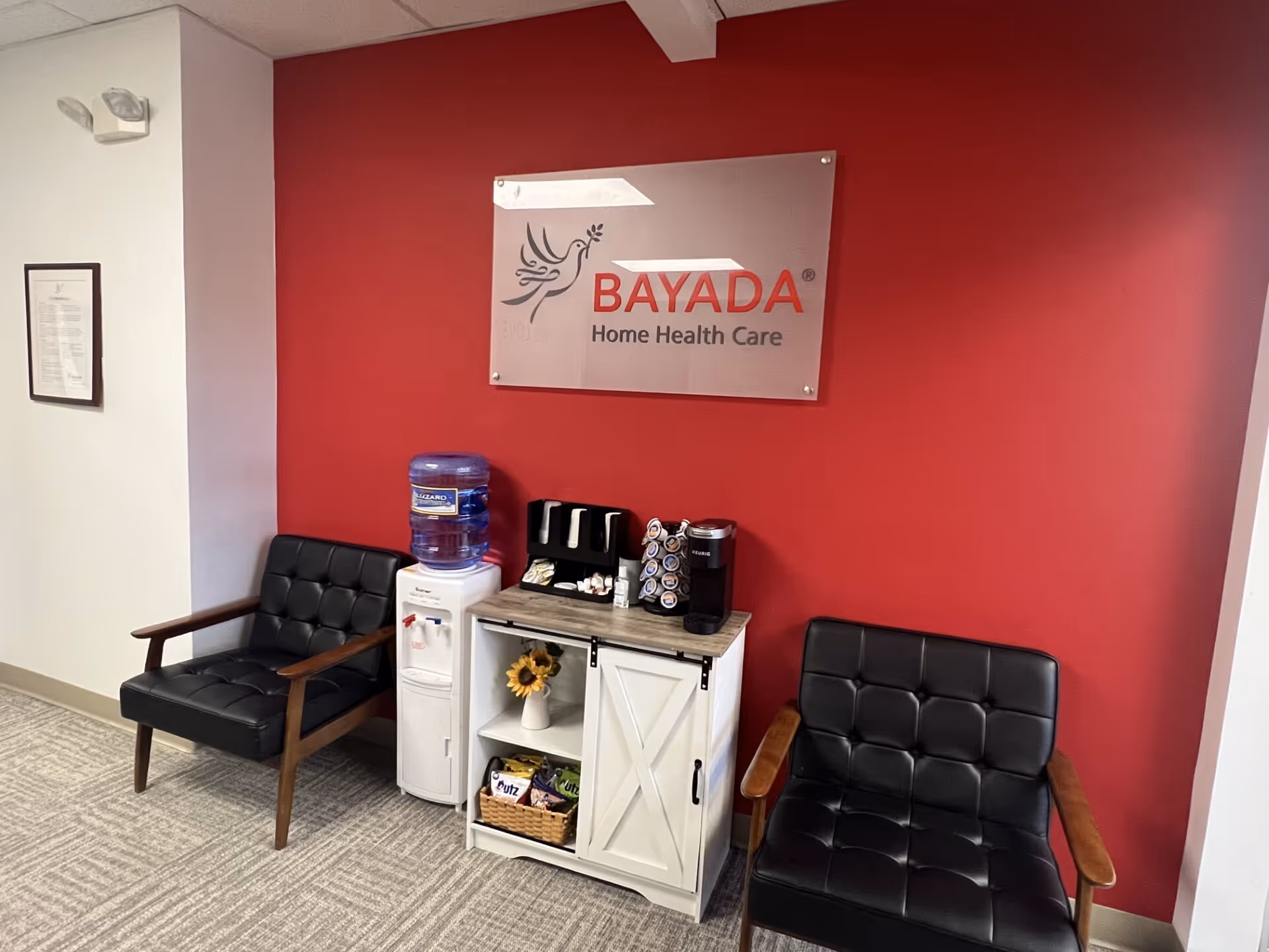 Lobby seating area against a red wall with BAYADA sign, water cooler, and coffee station.