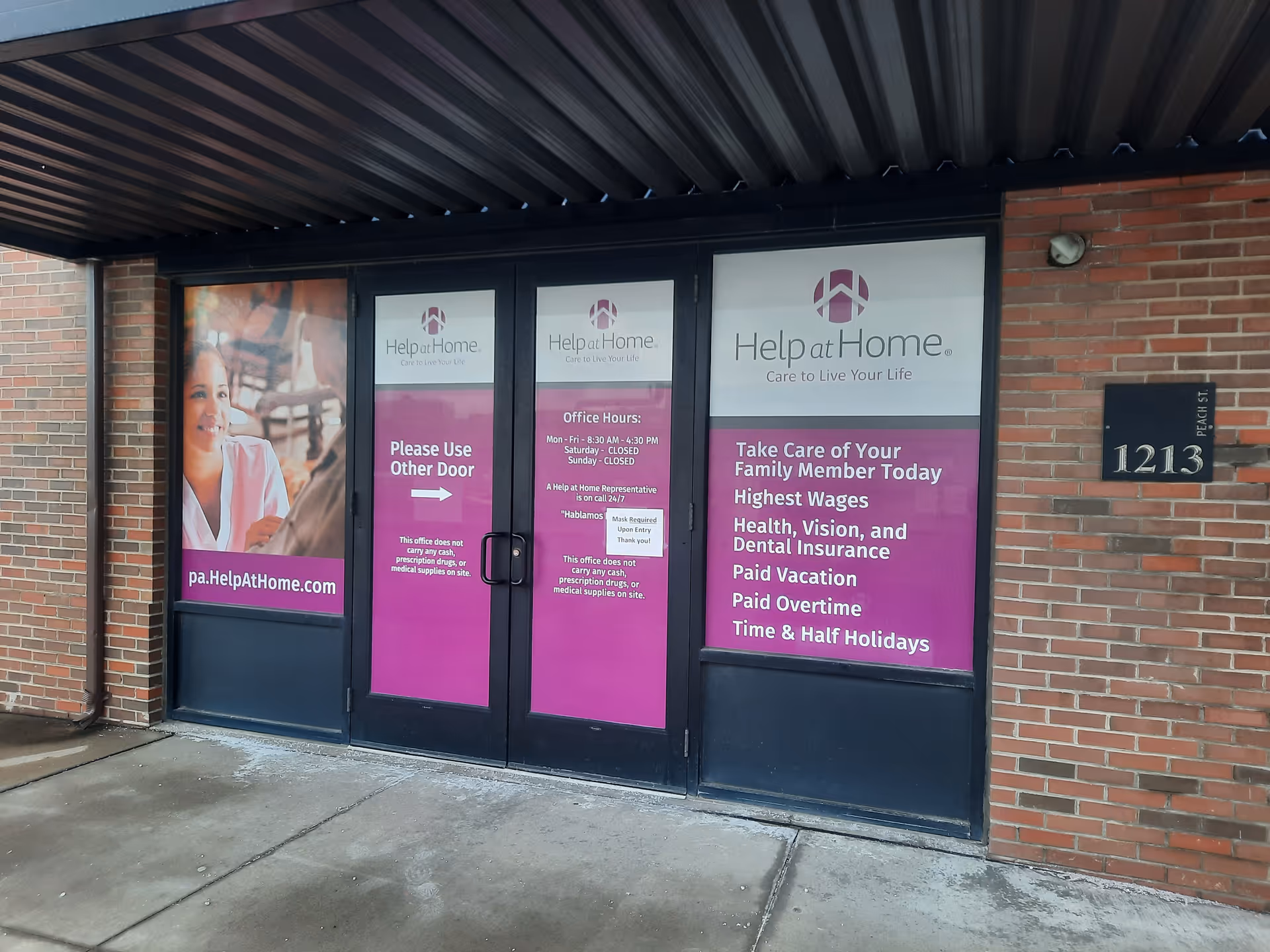 Front entrance of Help at Home facility with purple signs on glass doors and brick exterior.