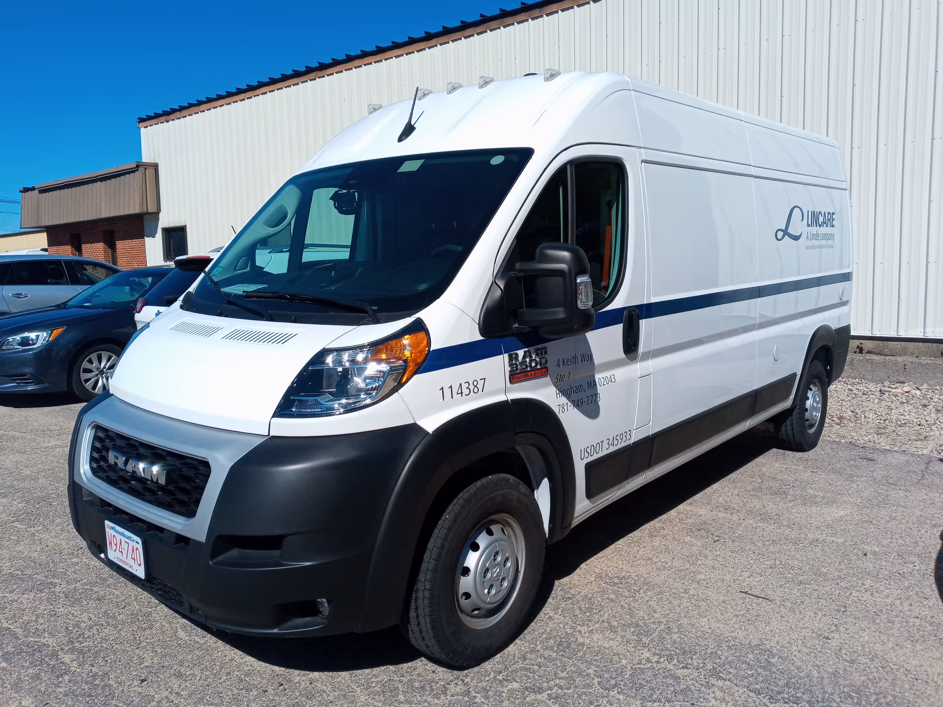 A white LINCARE transport van parked outdoors in a lot beside a large building.