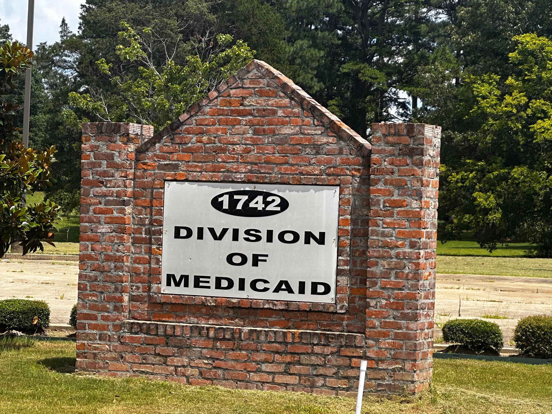 Brick sign reads '1742 Division of Medicaid' with trees and grass in background.