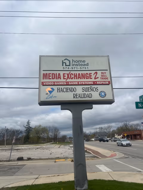 A roadside signboard on a pole advertising Media Exchange 2 with Home Instead branding.
