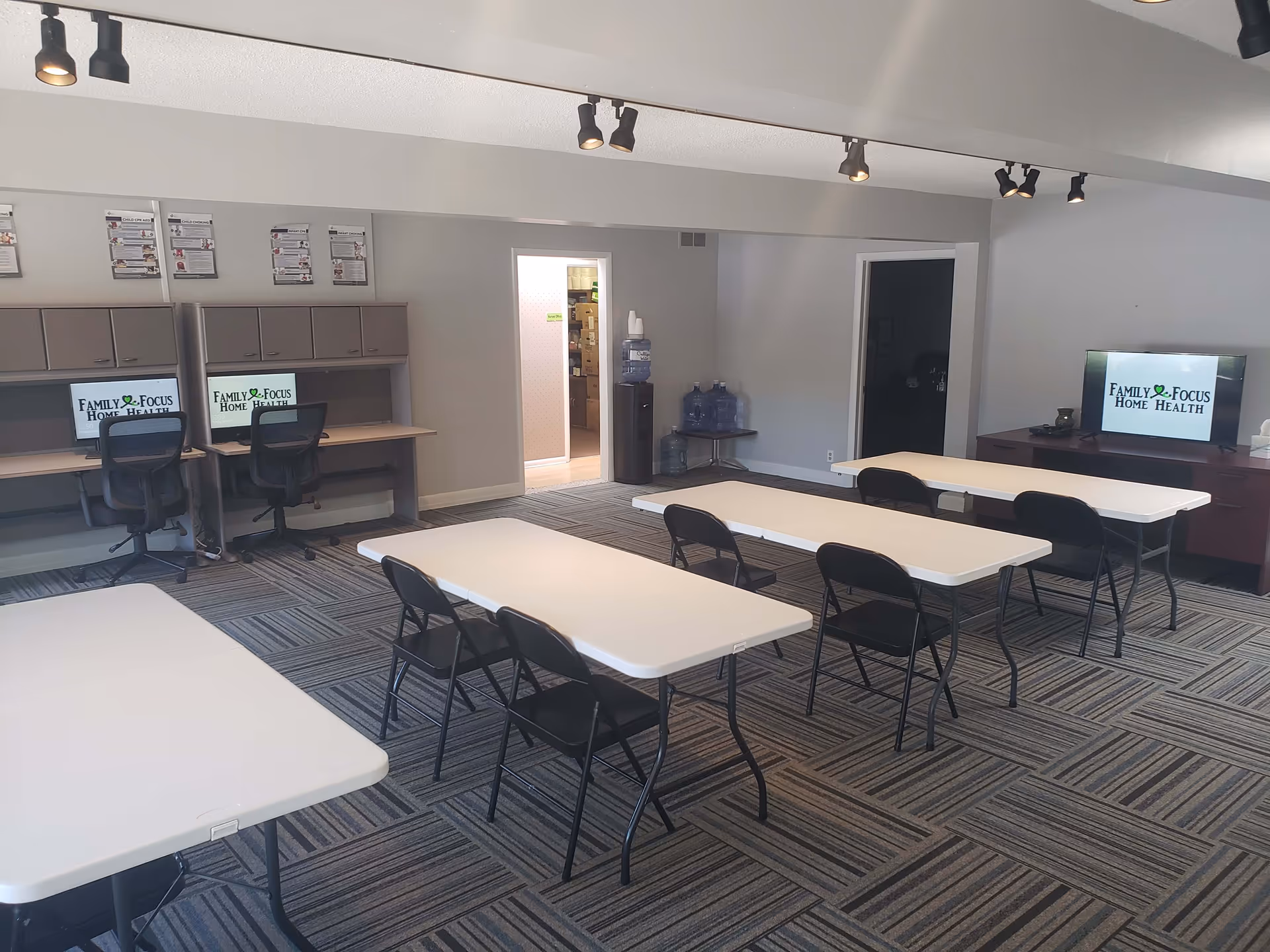 A large interior room with several white tables, black chairs, and computer stations along the wall.
