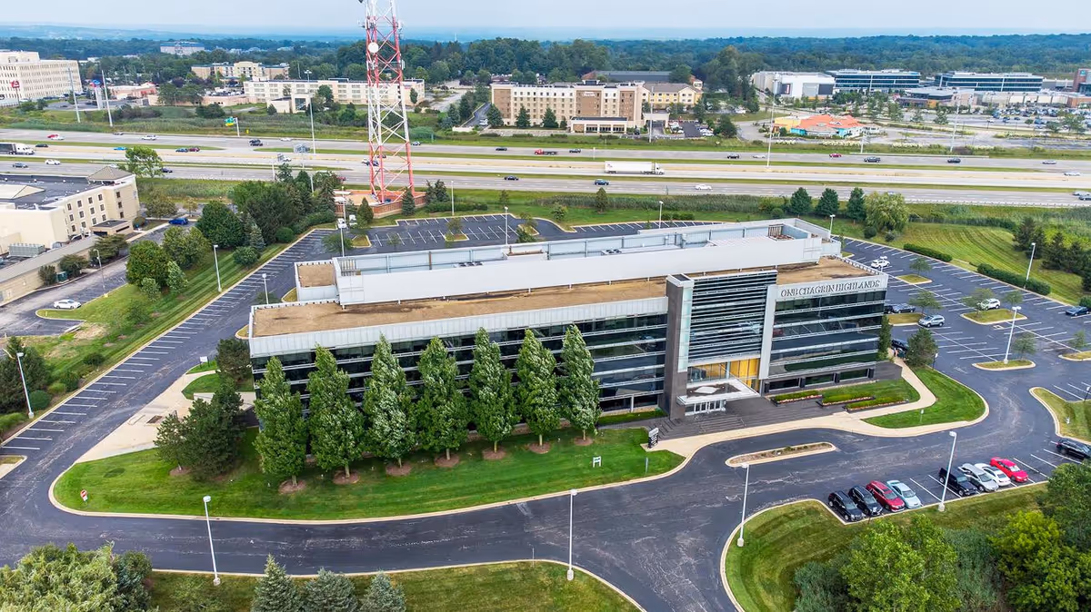 An aerial view of a modern senior living facility exterior surrounded by trees and parking.
