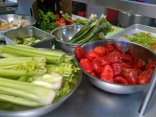 Assorted fresh vegetables in bowls on a stainless steel kitchen prep counter.