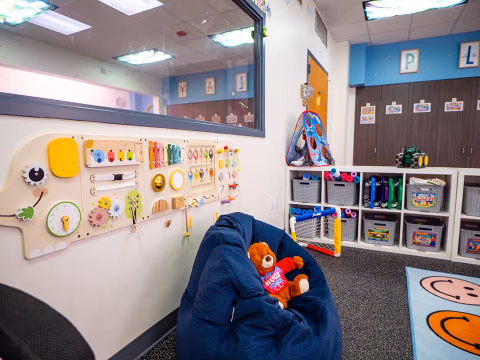 A colorful therapy playroom with a sensory board, bean bag, and cubby shelves.
