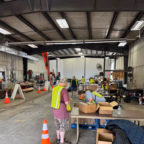Volunteers in reflective vests sort boxes inside a large warehouse workspace.