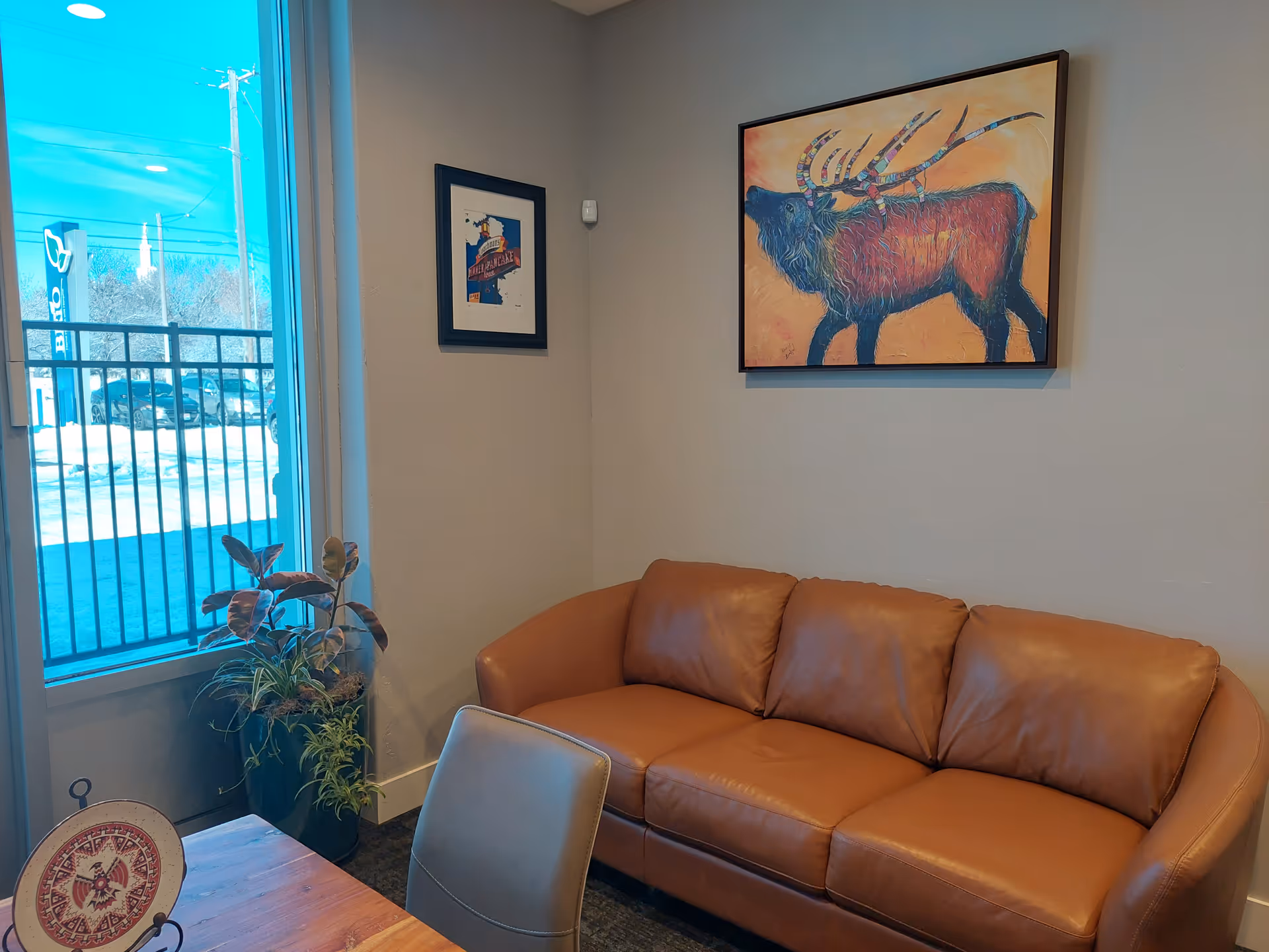 Cozy lobby seating area with tan leather sofa, plant, and colorful wildlife painting.