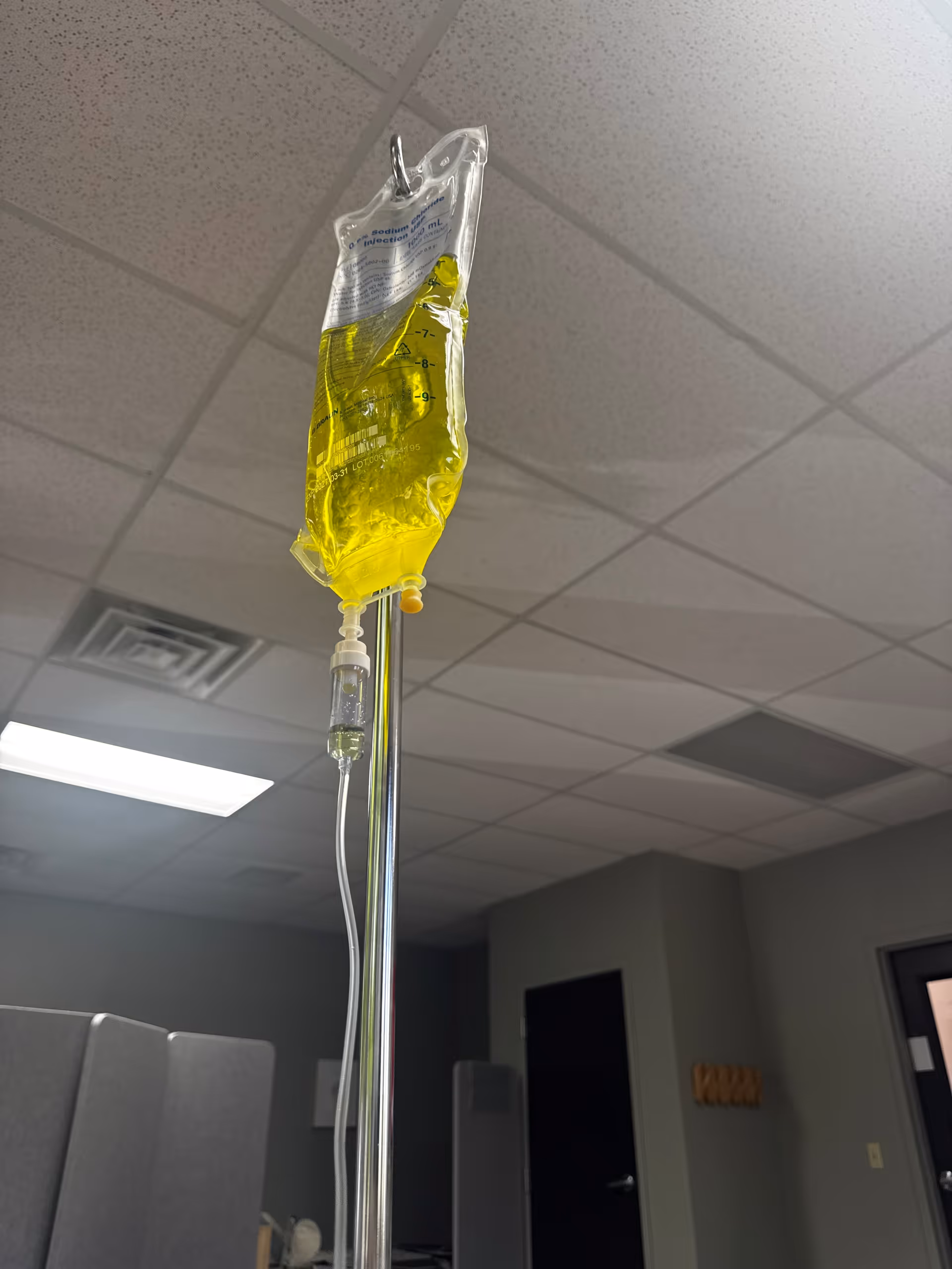 IV drip bag hangs from a pole in a hospital-like interior.