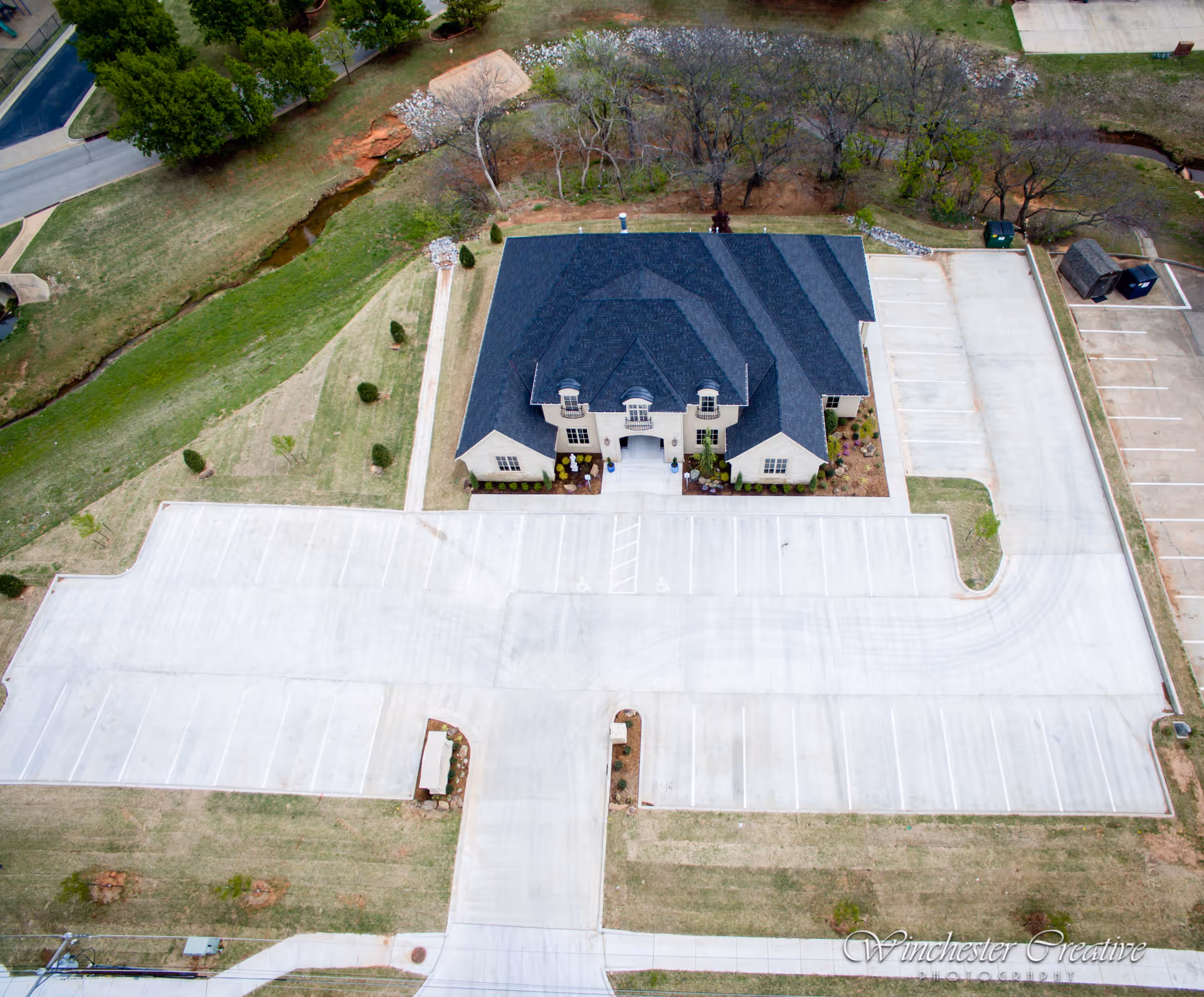 Aerial view of a large building with a dark roof and extensive parking.