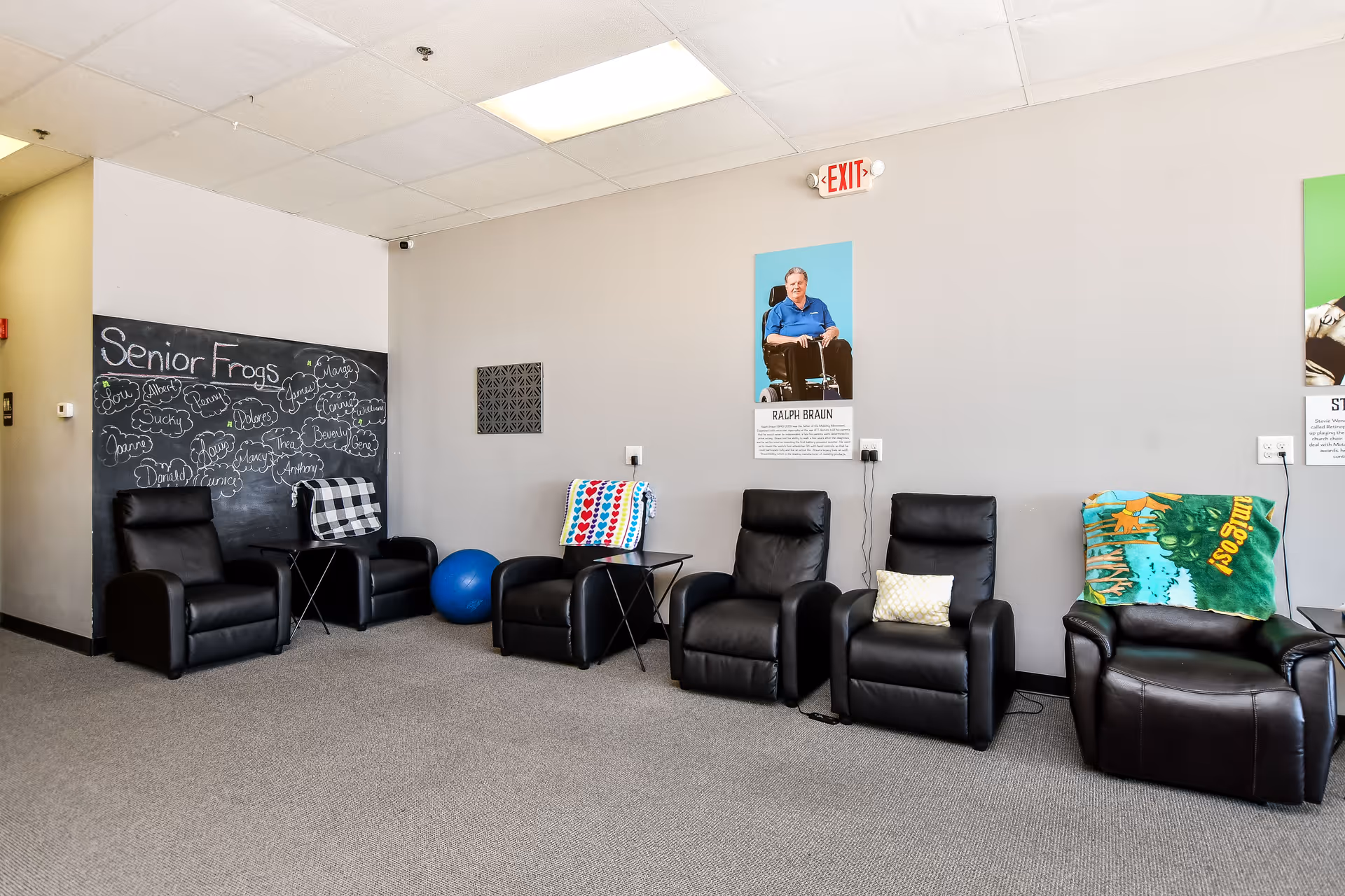 A row of black leather armchairs in a bright facility lounge with chalkboard wall.