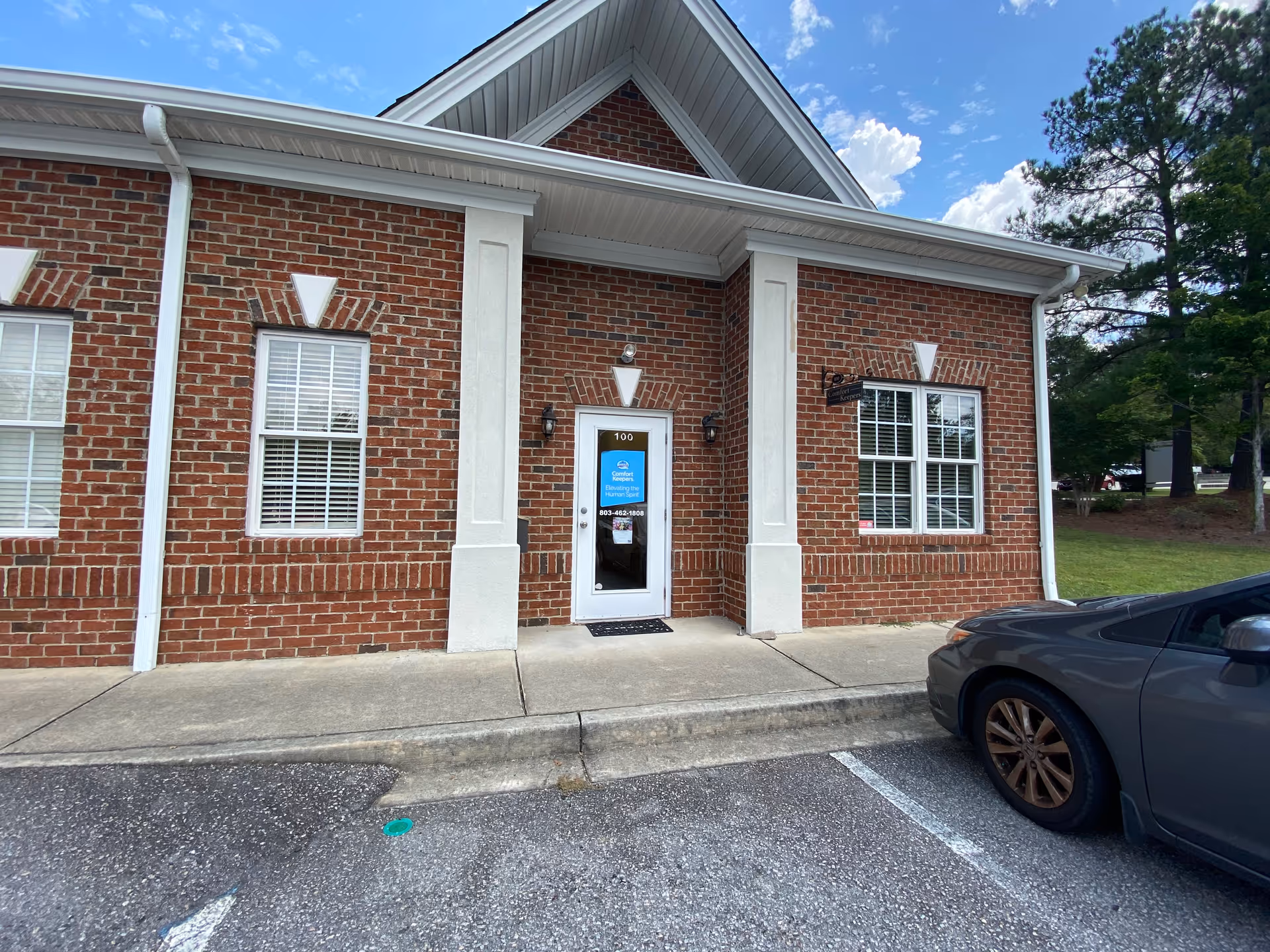 Front view of Comfort Keepers Home Care brick building with door and parked car.