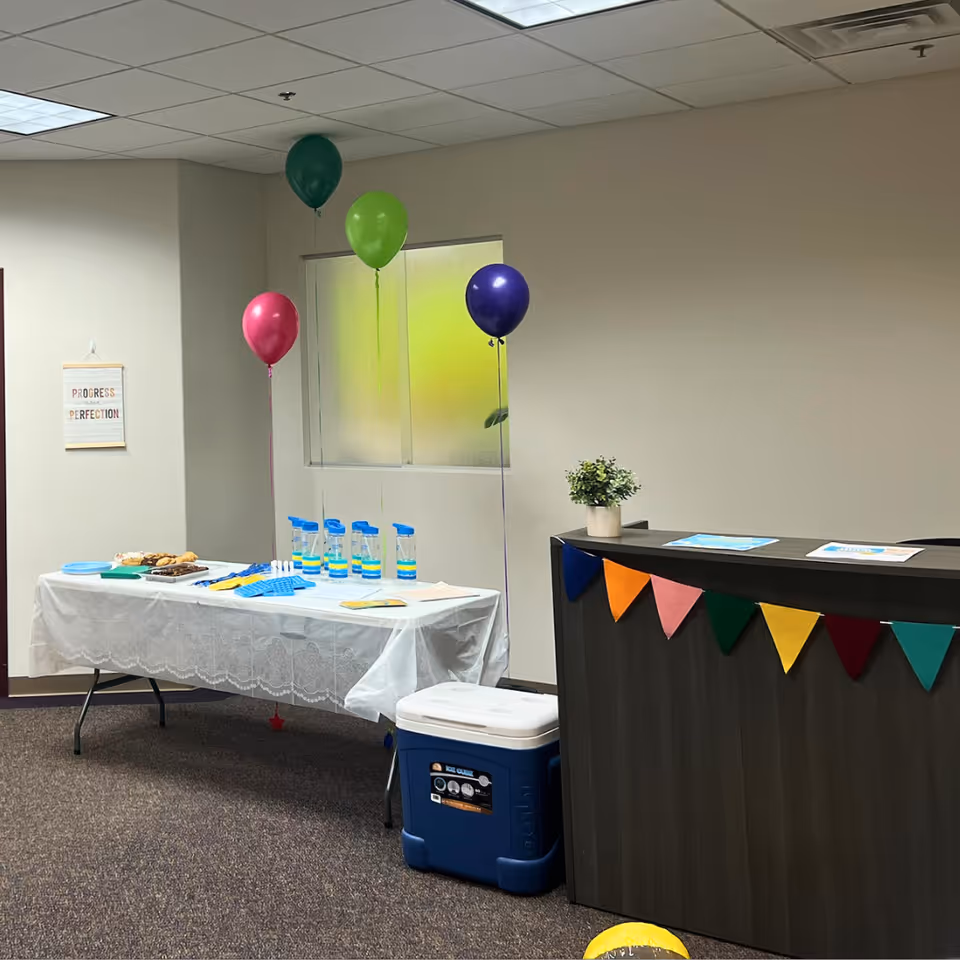 Indoor event setup with a snack table, water bottles, balloons, and a reception counter.