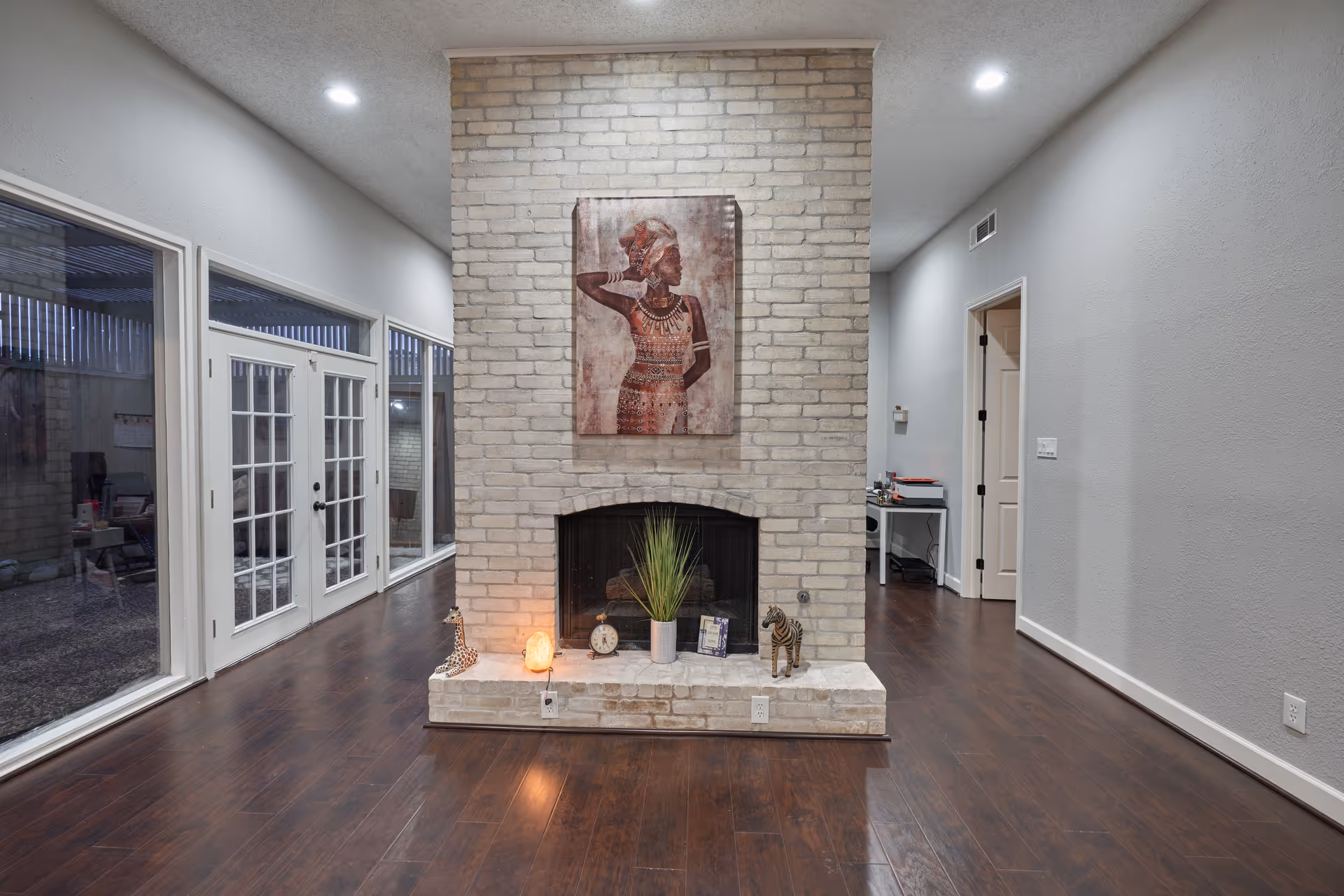 Modern living area featuring a brick fireplace, decor items, and glass doors along dark wood floors.