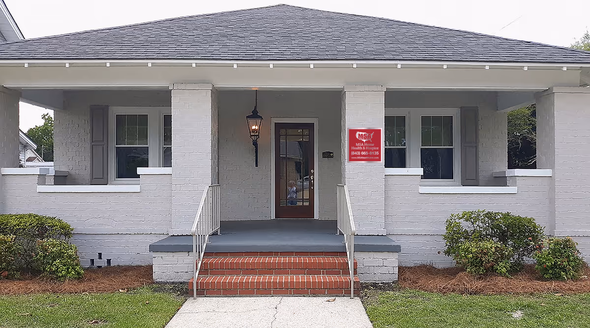 Front view of a single-story brick building with a porch, steps, and a doorway sign.