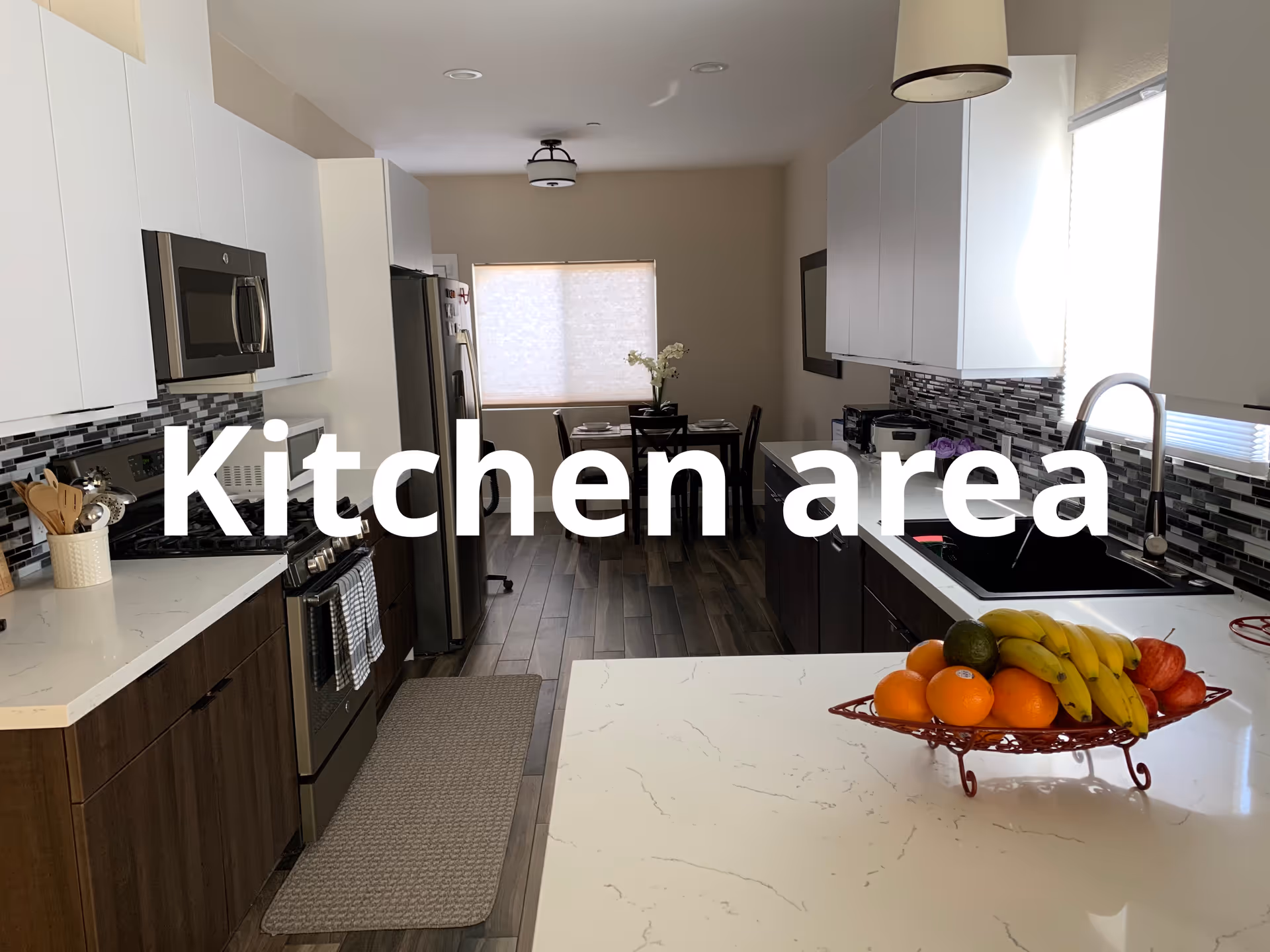 Modern kitchen area with white cabinets, stainless appliances, and a fruit basket on island.