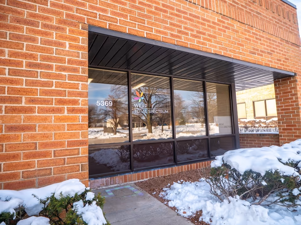Brick building storefront with glass windows, WEAP sign, and snowy landscaping.