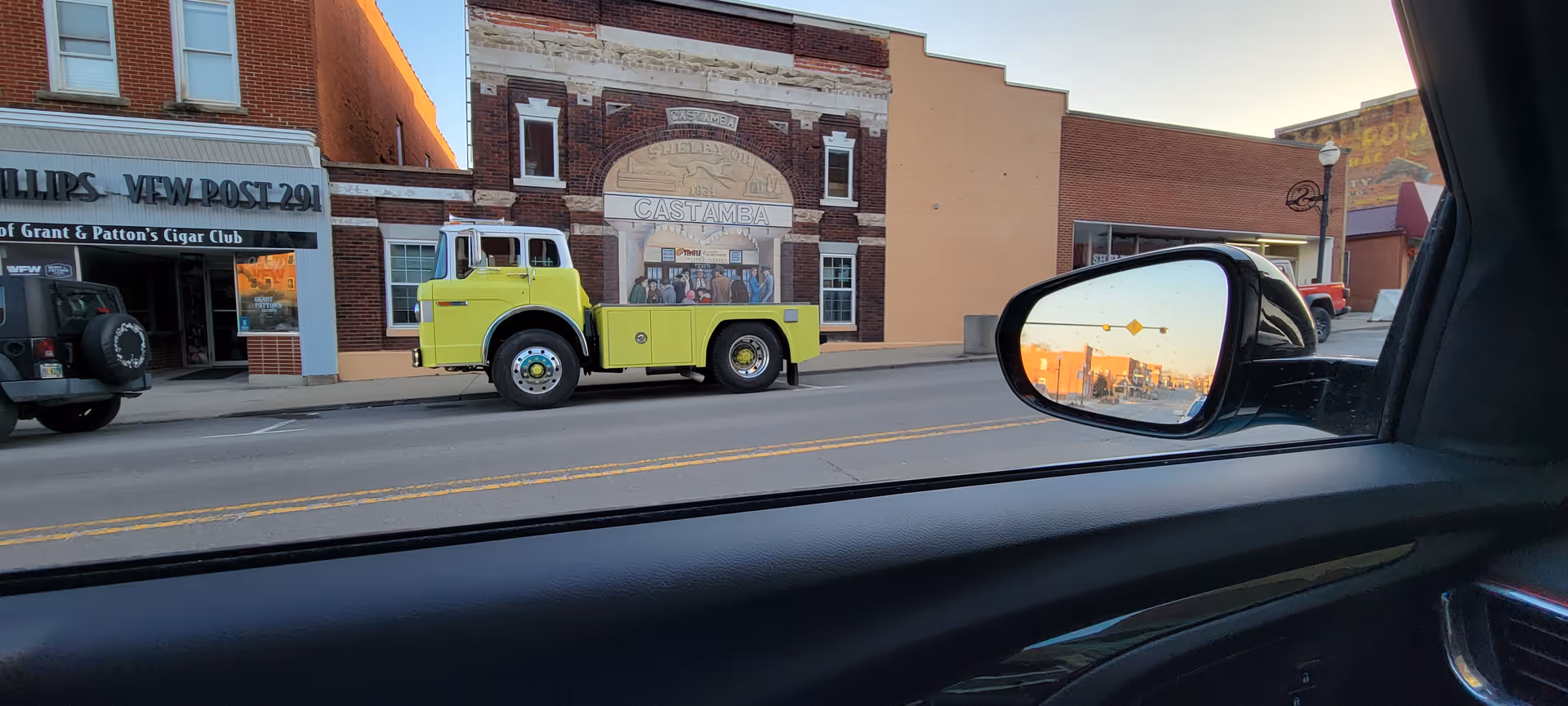 View from a car window of a street with a yellow fire truck and storefronts.