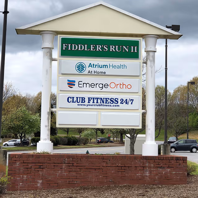 Outdoor sign structure displaying multiple business signs, including Atrium Health At Home.