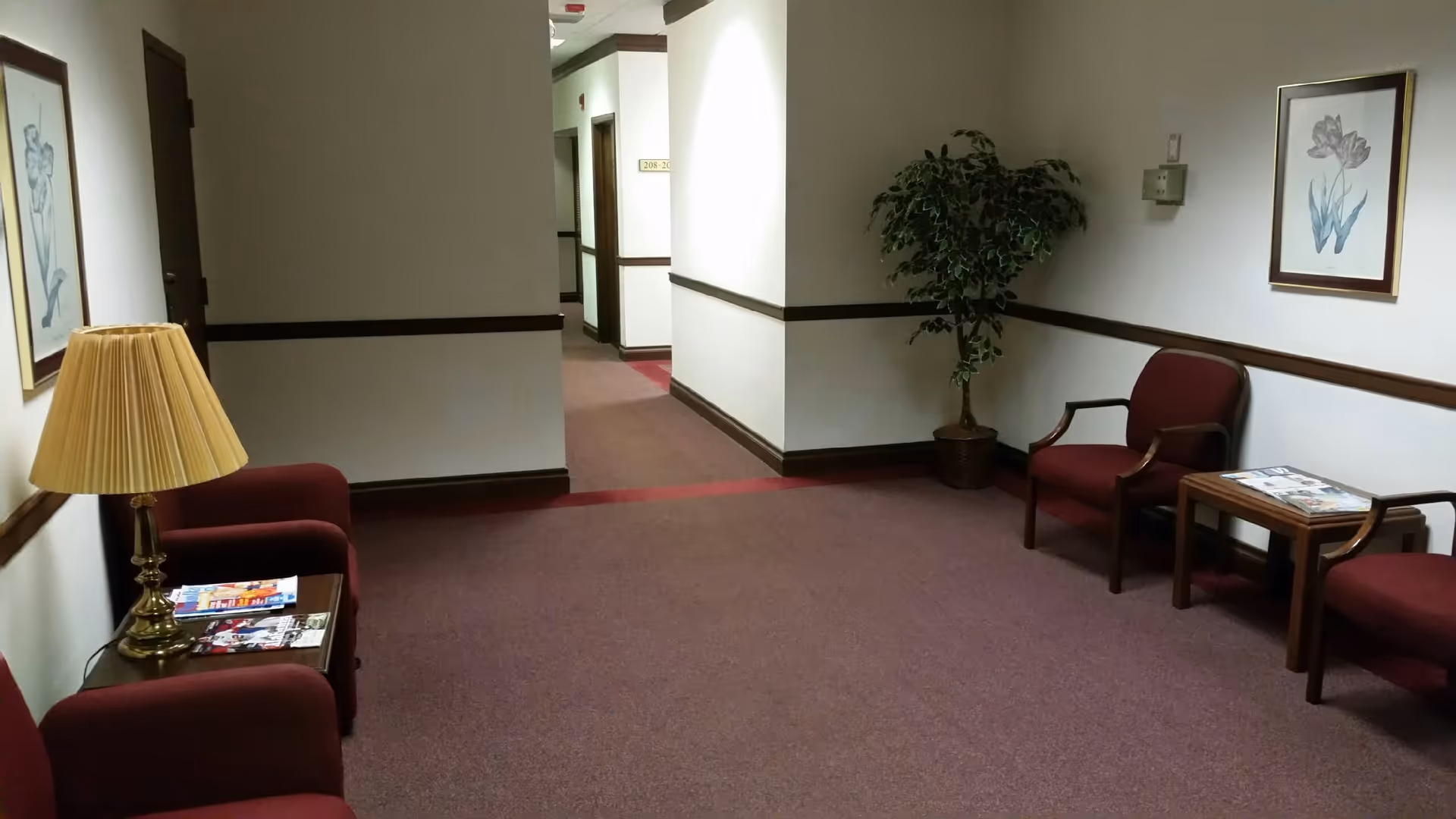 Indoor hallway of a senior living facility with chairs, a plant, and framed artwork.