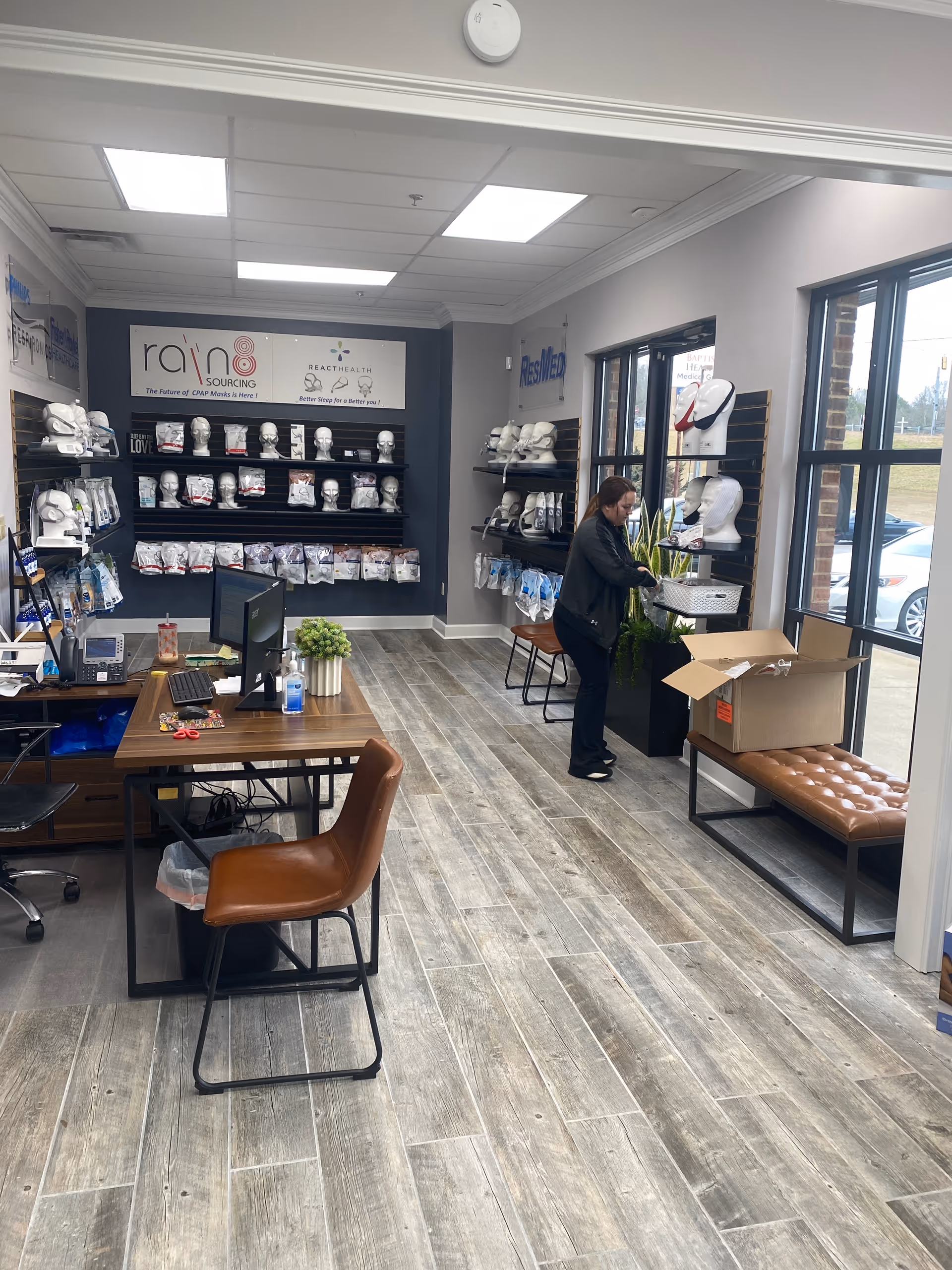 Interior view of a CPAP supply showroom with shelves, desks, and a worker near windows.