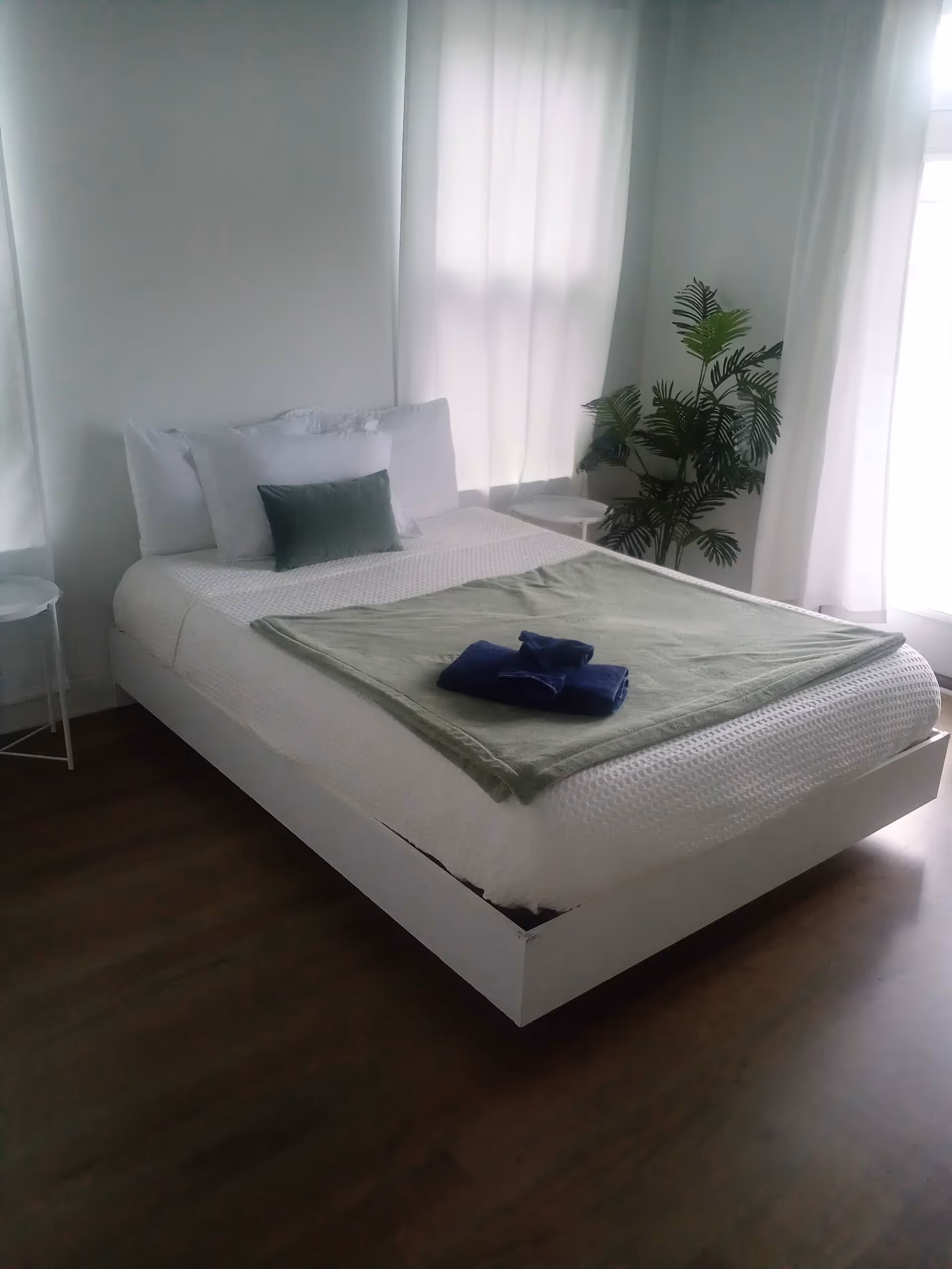 White bedroom with a bed, sheer curtains, and a potted plant.