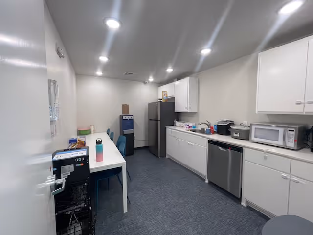 Bright white kitchen with cabinets, appliances, and a table with chairs along the left.