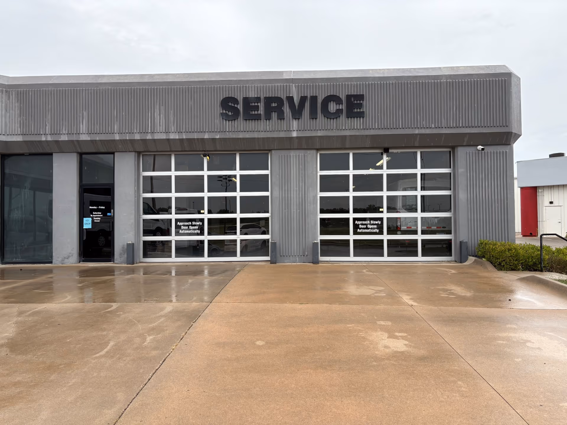 Exterior view of a service facility with large glass garage doors and a 'SERVICE' sign.