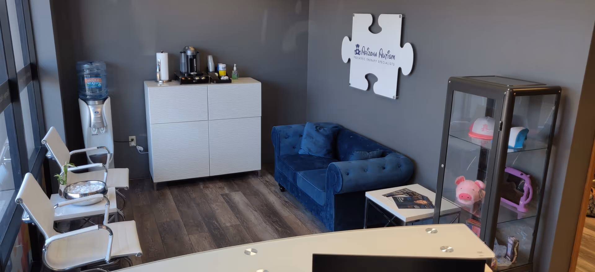Modern interior lounge with blue sofa, white cabinet, water cooler, and glass display cabinet.