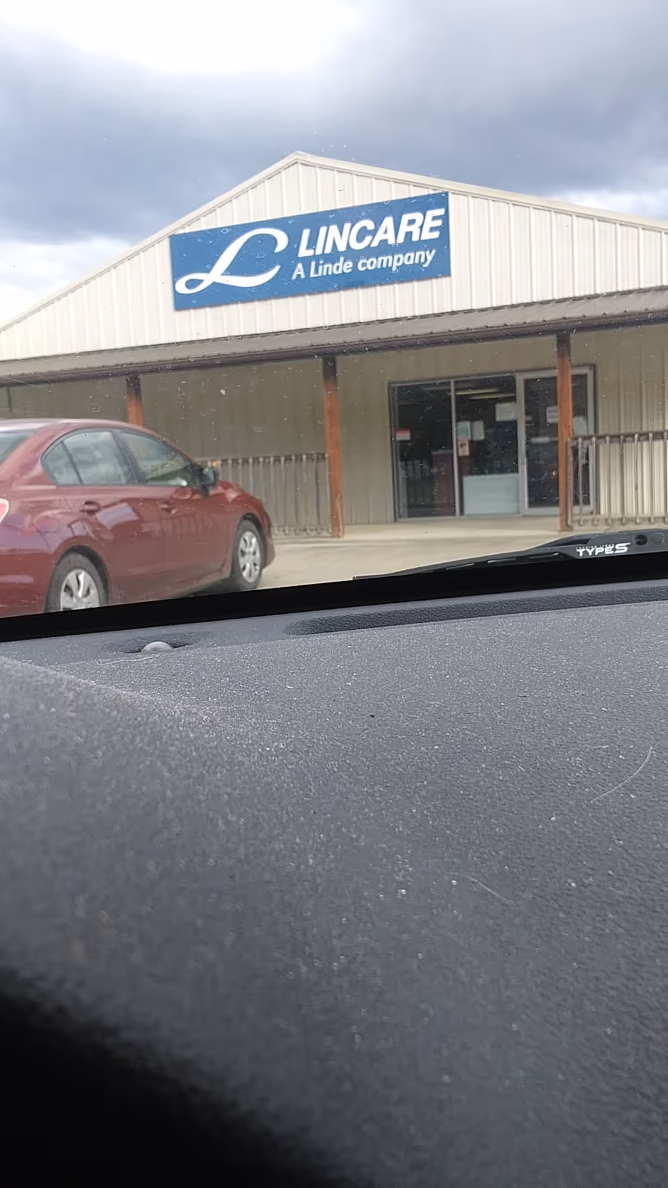 Front view of a LINCARE facility exterior with sign and a red car parked outside.