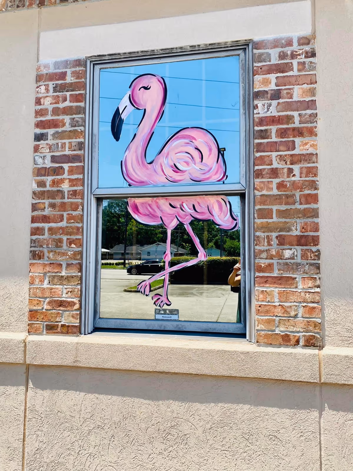 Pink flamingo mural painted on a glass window of a brick exterior wall.